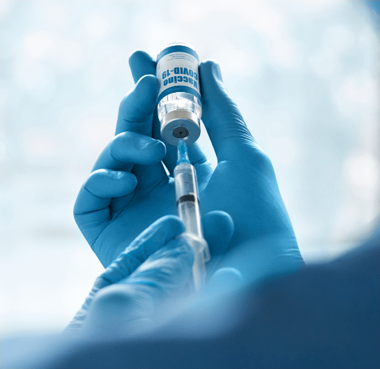 Hands with gloves drawing from a vial with a syringe.