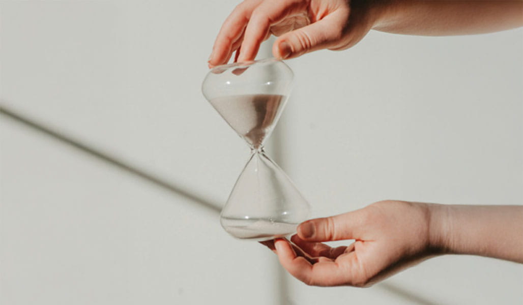 A person holds a clear glass hourglass.