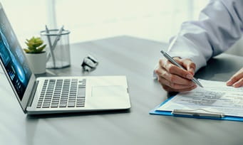 Consultant working on documents related to clinical strategy and planning with his laptop open in front of him