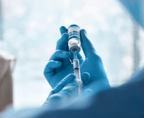 Healthcare professional withdrawing from a vial using a syringe.