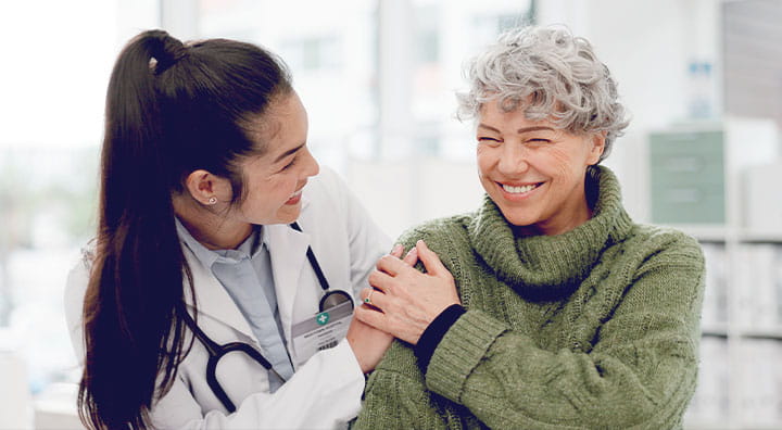 A healthcare professional in a lab coat comforts an elderly patient wearing a green sweater.