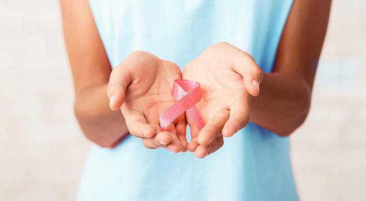 A woman holding a pink ribbon in her hands, symbolizing support and awareness for breast cancer.