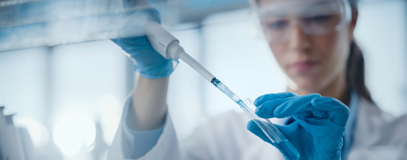 A female scientist in a lab coat holds a tube, conducting experiments in a laboratory setting.