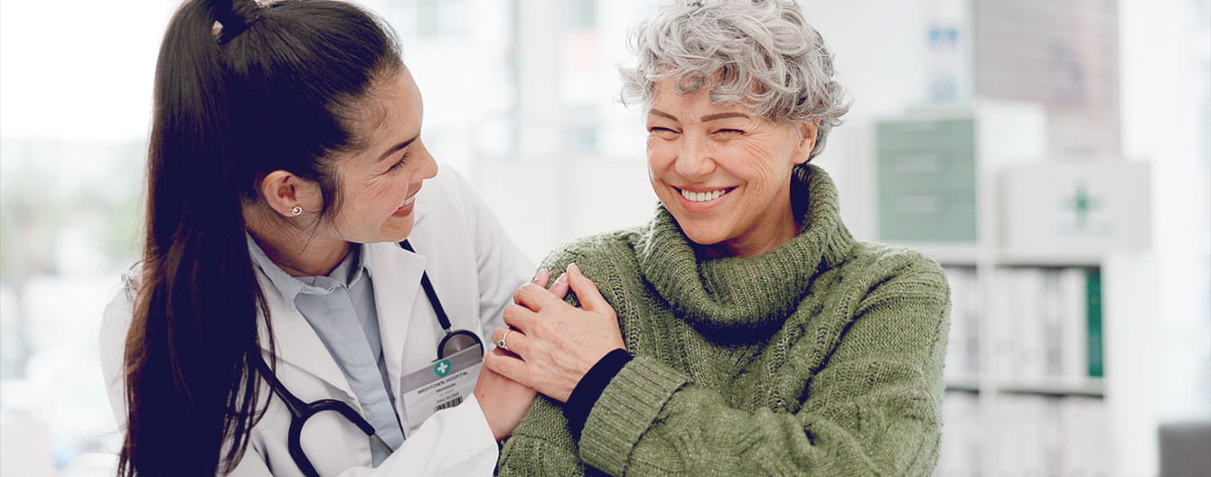 A healthcare professional in a lab coat comforts an elderly patient wearing a green sweater.