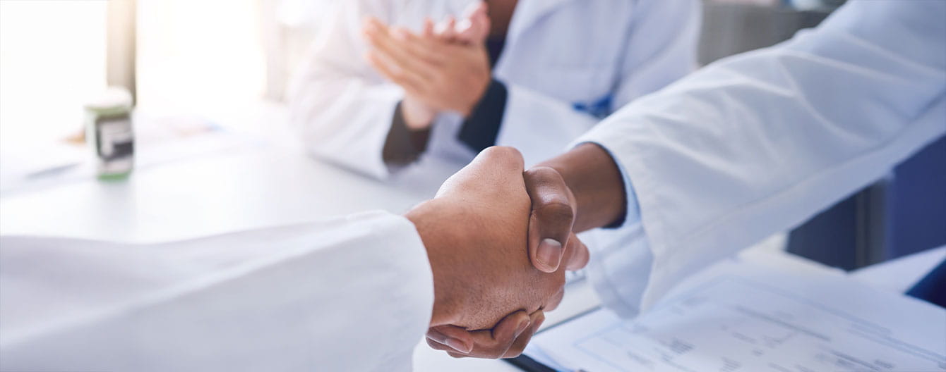 Doctors in white coats shake hands.