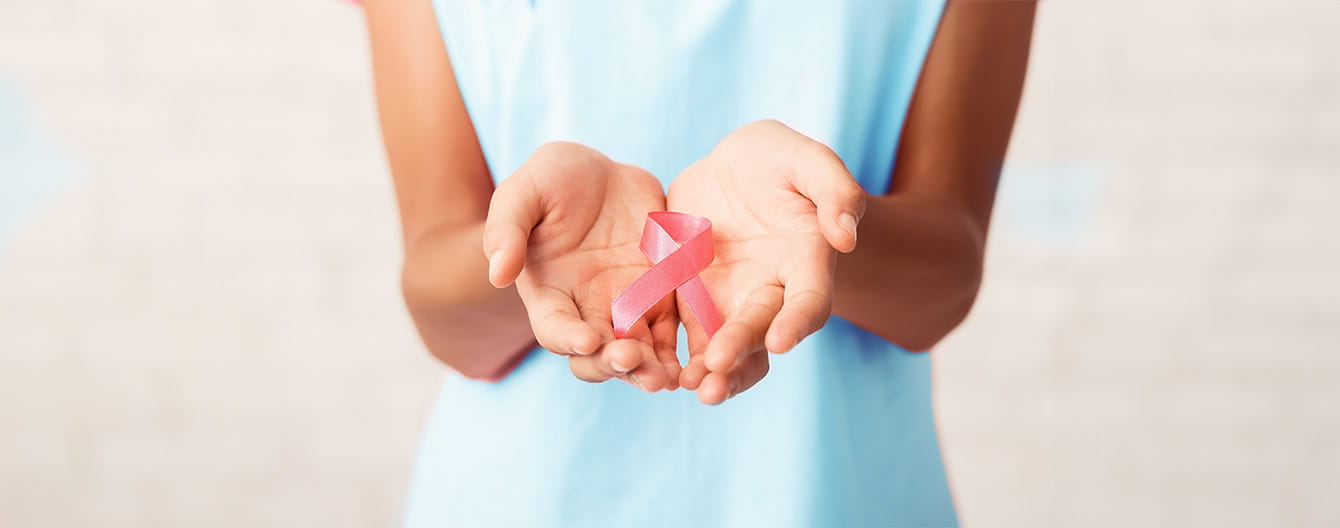 A woman holding a pink ribbon in her hands, symbolizing support and awareness for breast cancer.