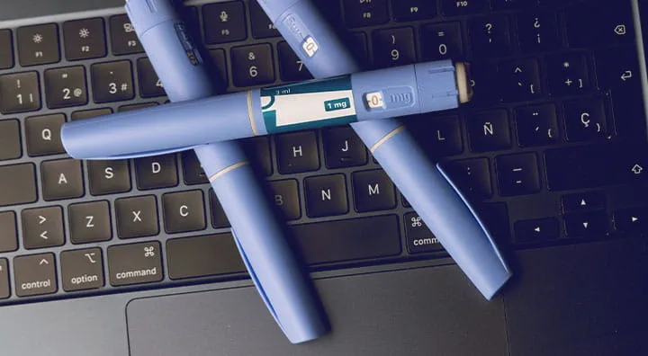 蓝色医用注射笔放在黑色笔记本电脑键盘上。
